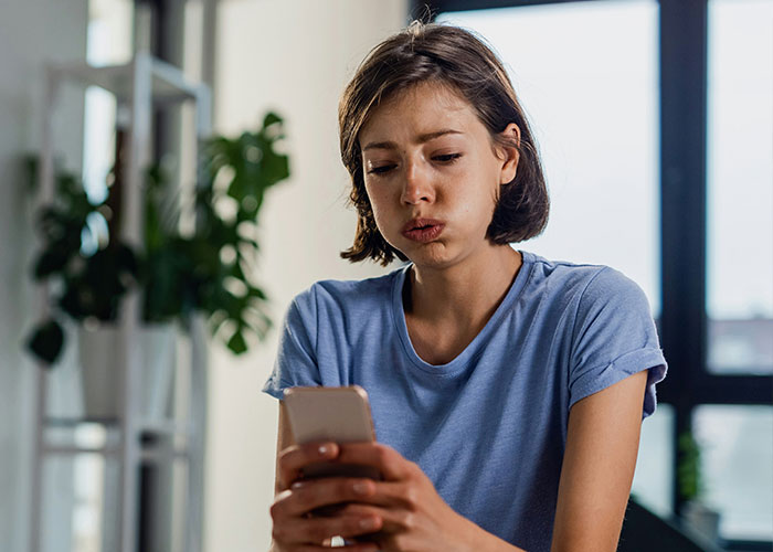 Woman in blue shirt looking at her phone, appearing shocked by a savage insult.