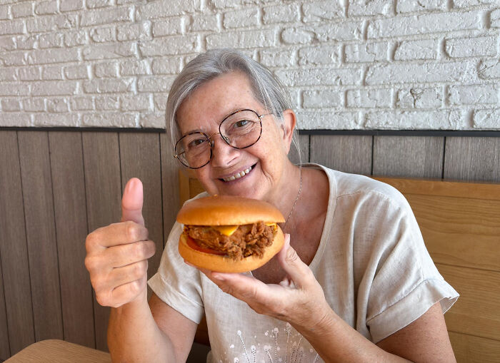 Woman smiling, holding a burger, giving thumbs up; discussing iron levels and quitting veganism.