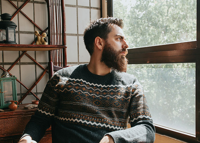 Man gazing out the window, reflecting on struggles men wish women knew, wearing a patterned sweater.