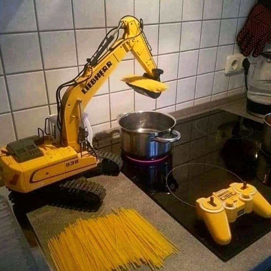 Toy excavator lifting spaghetti into a pot on the stove, demonstrating a playful concept that goes hard.