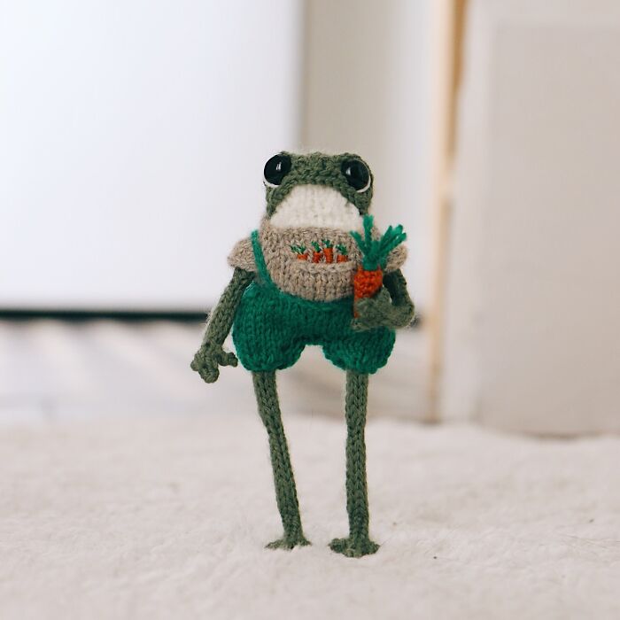 Miniature knitted frog in green shorts holding a carrot, crafted by a French knitter.
