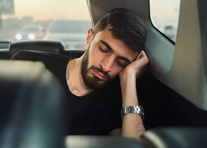 Man sleeping in a car, illustrating struggles men wish women knew, wearing a black shirt with a watch showing peaceful rest.