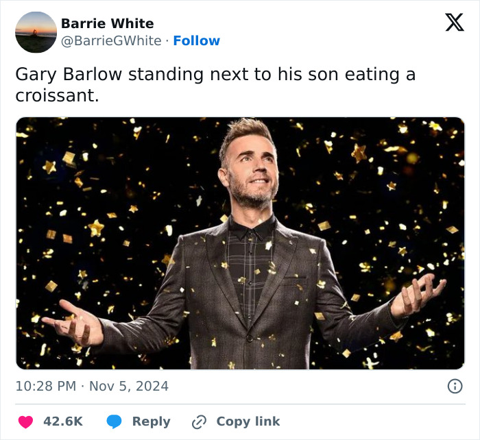 Gary Barlow under confetti, in a suit, smiling with outstretched arms.