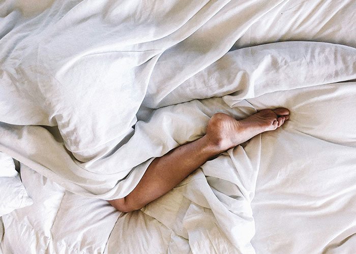 Bare foot sticking out of tangled white sheets, symbolizing understandable reasons for divorce.