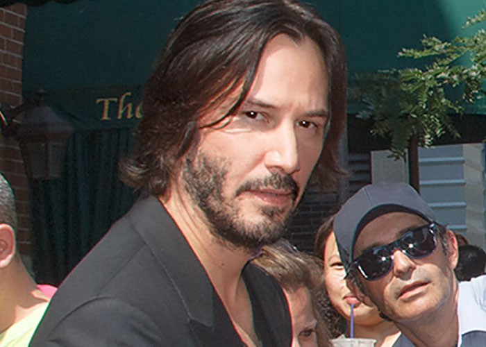 A man with medium-length hair and facial hair stands outdoors surrounded by fans.