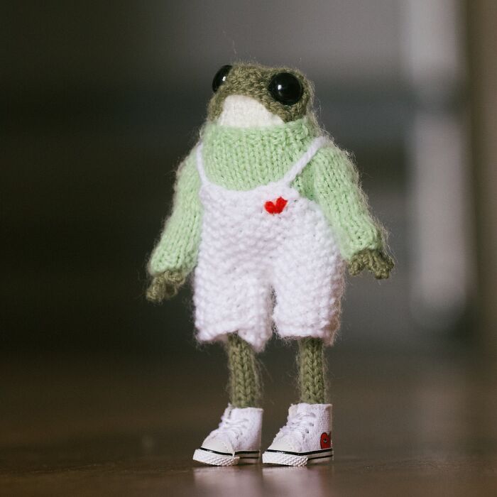 Miniature knitted frog in white overalls with a red heart, crafted by a French knitter, wearing tiny white sneakers.