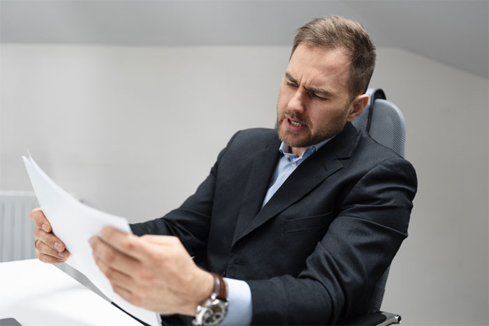 Man in a suit reading papers with a confused expression, representing inheritance surprise secrets. Man in a suit reading papers with a confused expression, representing inheritance surprise secrets.