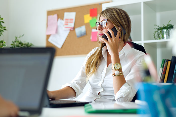 Recruiter on phone, looking concerned at a desk with a laptop, after ghosting a candidate during the hiring process.