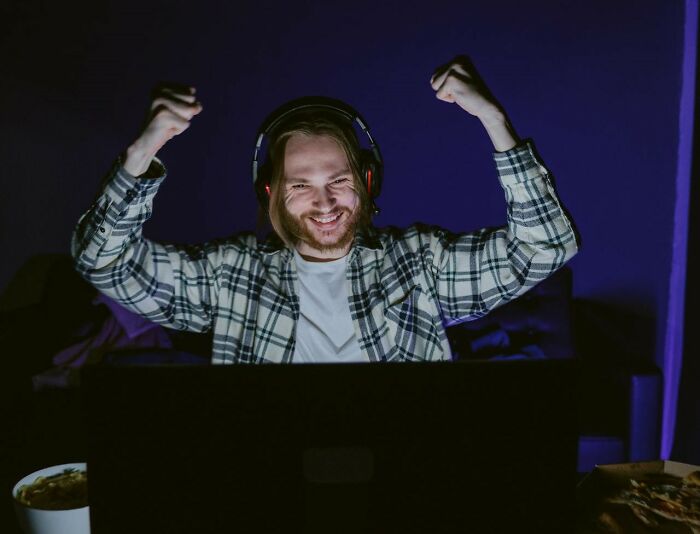 Person celebrating victory online, wearing headphones and a plaid shirt, embodying trust in numbers.
