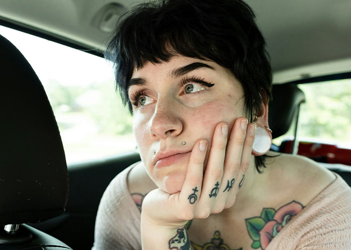 Person with tattoos inside a car, looking thoughtful, representing savage insults theme.