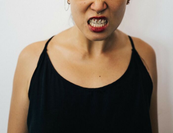 Woman clenching teeth, wearing a black top, expressing frustration related to cringy nice guy behaviors.