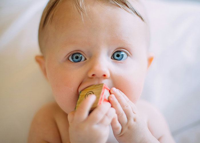 Baby with blue eyes chewing on a wooden block, representing childhood innocence amidst social challenges. Baby with blue eyes chewing on a wooden block, representing childhood innocence amidst social challenges.