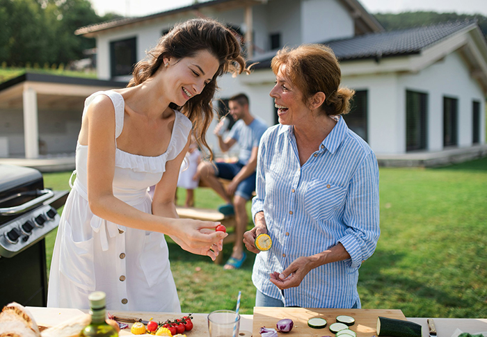 Woman and her mother-in-law preparing food outdoors, smiling and enjoying a sunny day, with focus on family interaction. Woman and her mother-in-law preparing food outdoors, smiling and enjoying a sunny day, with focus on family interaction.