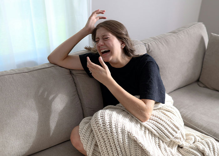 Woman emotionally distraught, illustrating struggles men wish women knew, sitting on a couch wrapped in a blanket.
