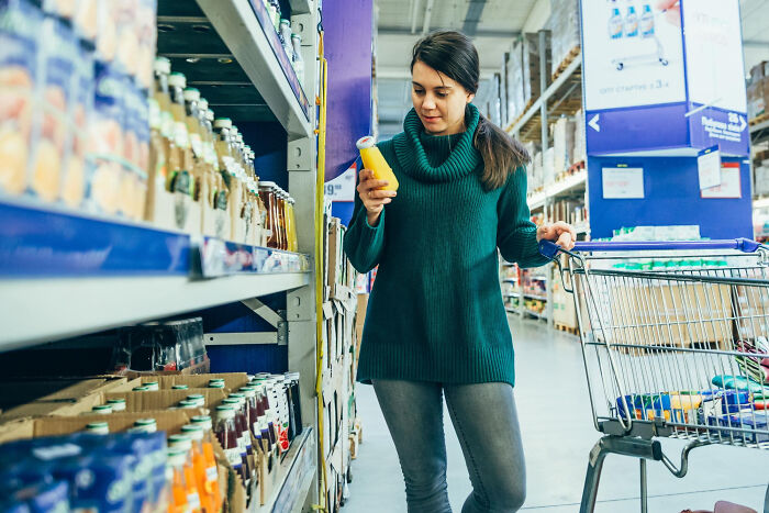 Woman experiencing reverse culture shock in a grocery store, examining a juice bottle while shopping.