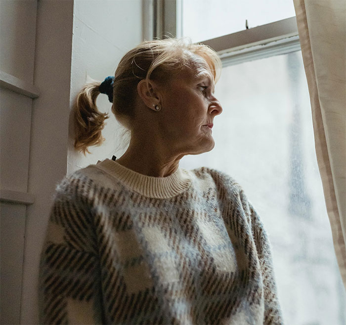 Woman looking thoughtful out the window, dressed in a patterned sweater, pondering her daughter-in-law's secrecy. Woman looking thoughtful out the window, dressed in a patterned sweater, pondering her daughter-in-law's secrecy.