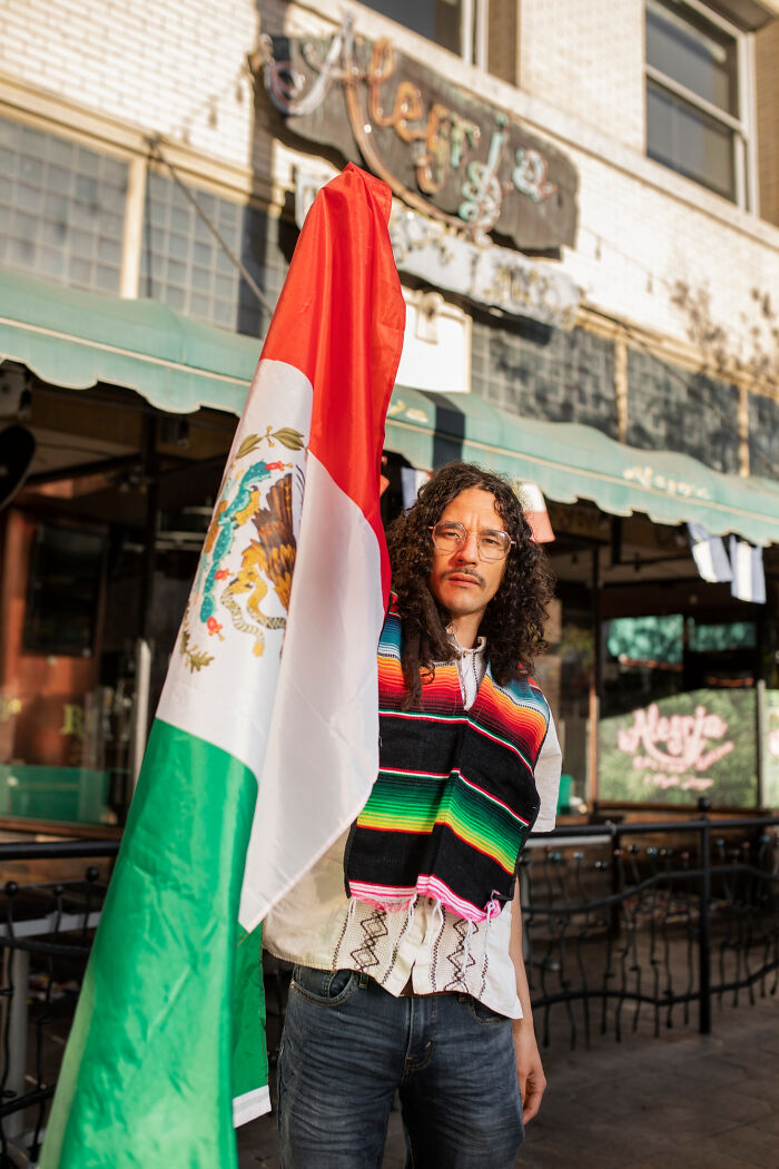 Person holding Mexican flag outside a restaurant, highlighting cultural pride in a colorful setting.