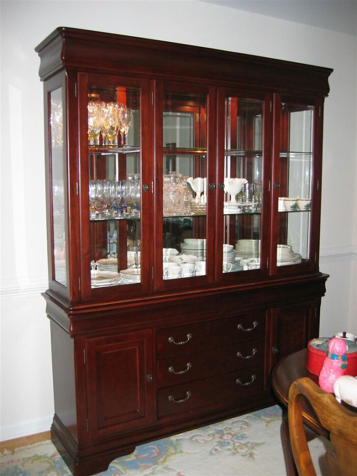 A vintage china cabinet, once a symbol of luxury, filled with glassware and dishes, now considered obsolete in modern homes.
