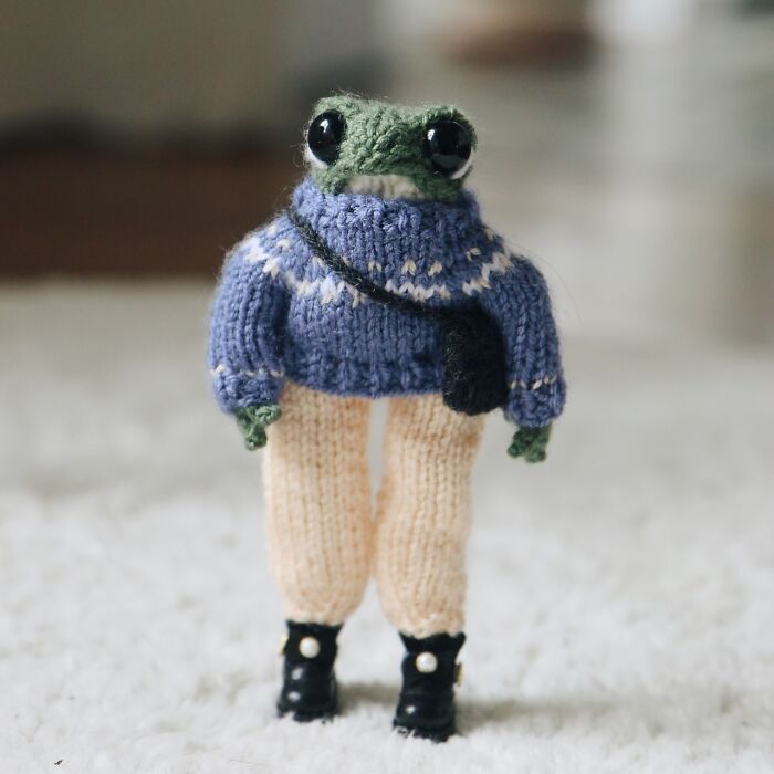 Miniature knitted frog in cozy sweater and boots on soft carpet.