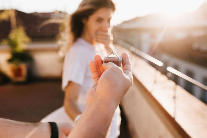 A person proposing with a ring box on a rooftop, capturing a risky decision moment.