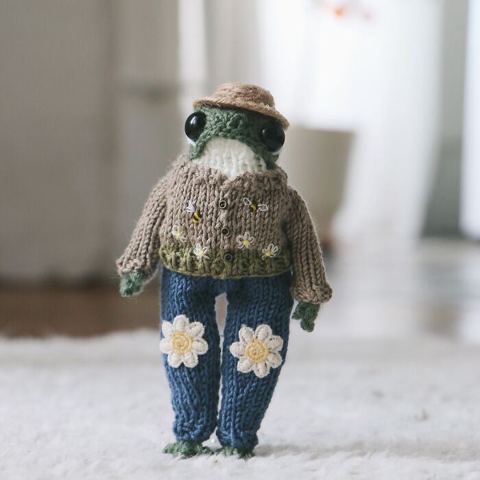 Knitted miniature frog in a sweater and jeans with flowers, created by a French knitter.