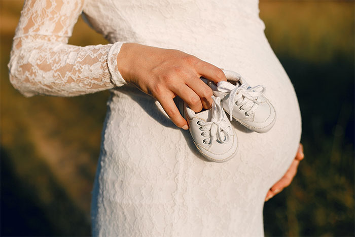 Pregnant woman in lace dress holding baby shoes, symbolizing family secrets and inheritance revelations. Pregnant woman in lace dress holding baby shoes, symbolizing family secrets and inheritance revelations.
