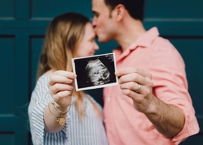Couple holding an ultrasound photo, with the man kissing the woman's forehead, symbolizing future parenting challenges. Couple holding an ultrasound photo, with the man kissing the woman's forehead, symbolizing future parenting challenges.