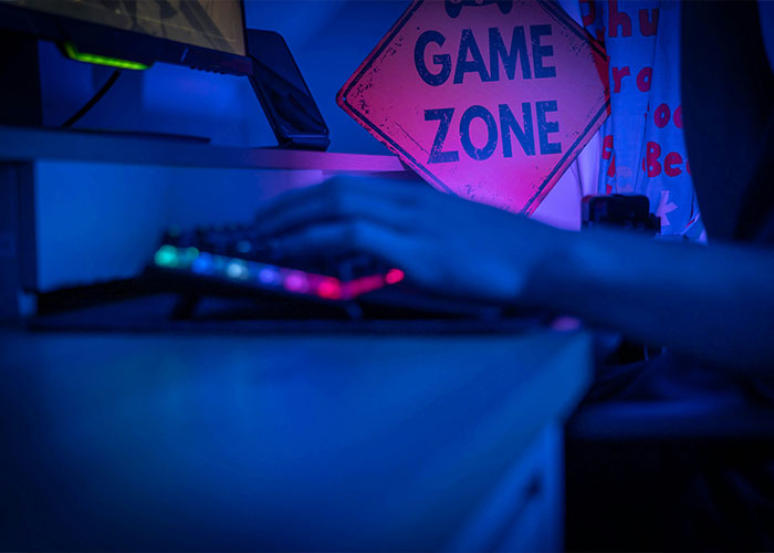 Person typing on a keyboard in a dimly lit room, with a "Game Zone" sign, representing reasons for divorce.
