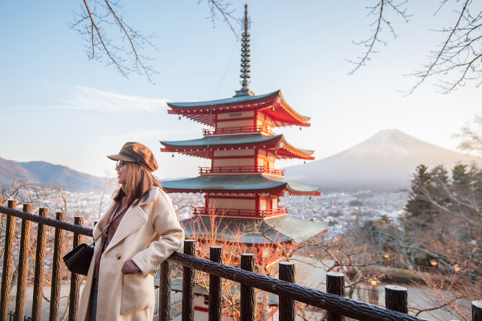 Woman in a coat and hat in front of a pagoda and Mount Fuji at sunset, reflecting on a risky decision.