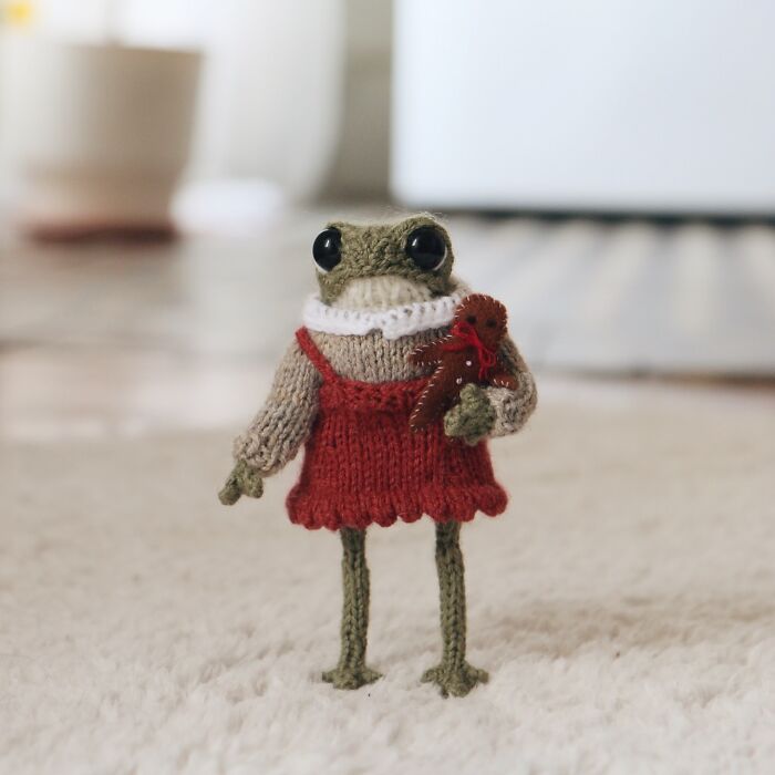 Miniature knitted frog in a red dress, created by a French knitter, holding a small teddy bear.