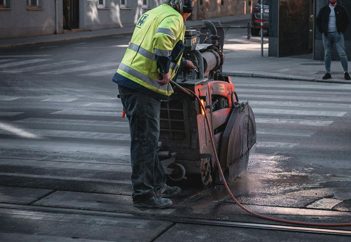 Worker quickly operating machinery on a street, illustrating malicious compliance with safety gear. Worker quickly operating machinery on a street, illustrating malicious compliance with safety gear.
