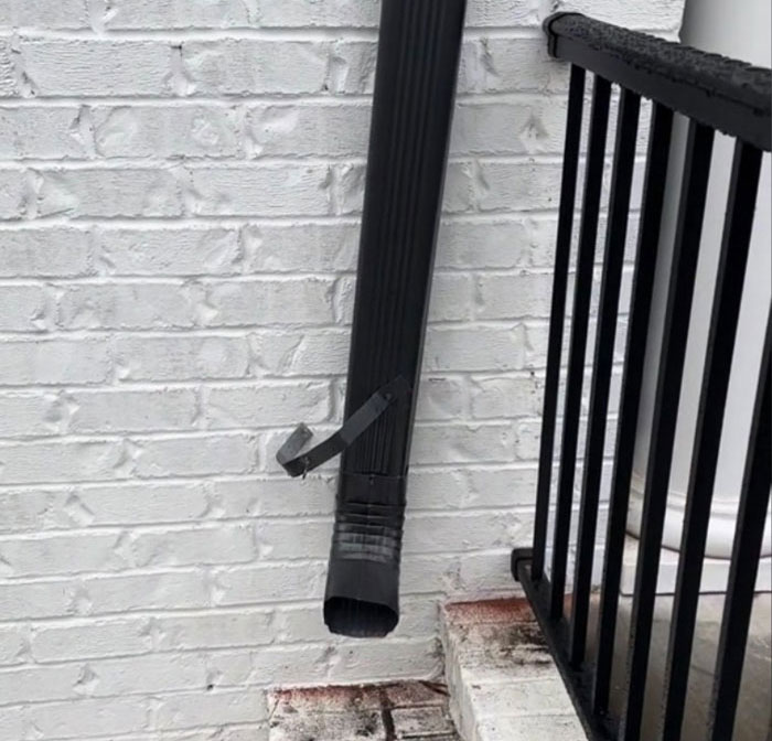 Downspout duct-taped to a brick wall on a $1,600,000 home built 2 years ago, illustrating poor construction condition.