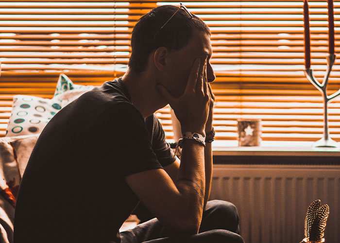 Man sitting indoors with his hand on his face, illustrating struggles men experience.