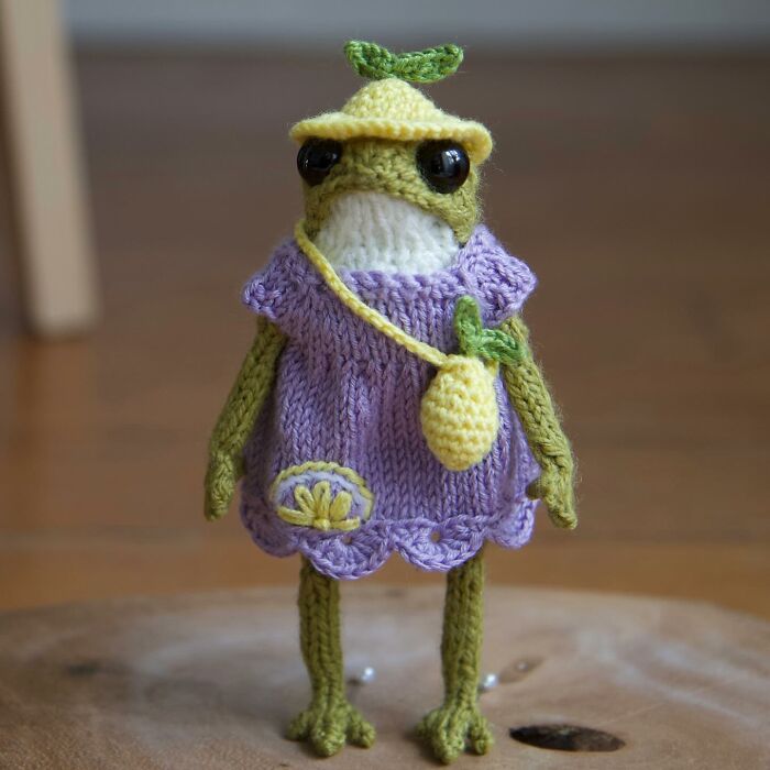 Knitted miniature frog in a purple dress with a yellow hat, created by a French artist.