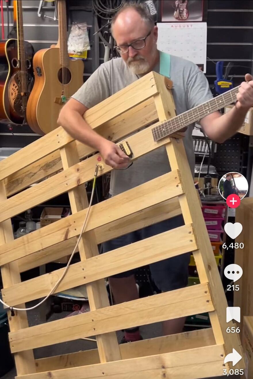 Man playing a unique pallet guitar in a workshop, showcasing creative musical innovation and 'pics that go hard'.