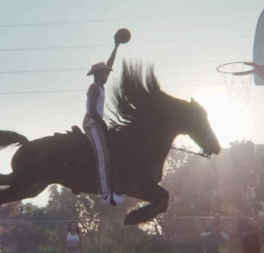 Rider on a horse performs a basketball dunk at sunset, capturing a cool moment.