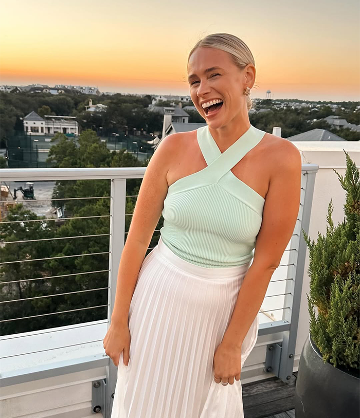 Influencer in mint top and white skirt on a balcony at sunset.