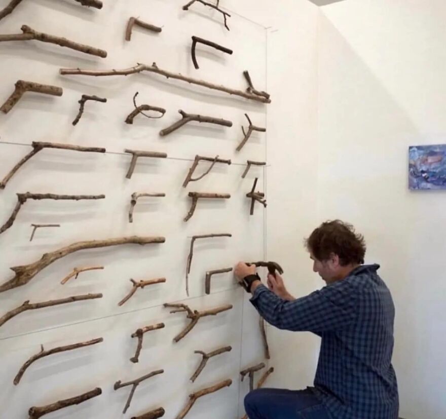 Person arranging branches on a wall display; showcasing a creative and unique composition in "Pics That Go Hard" style.