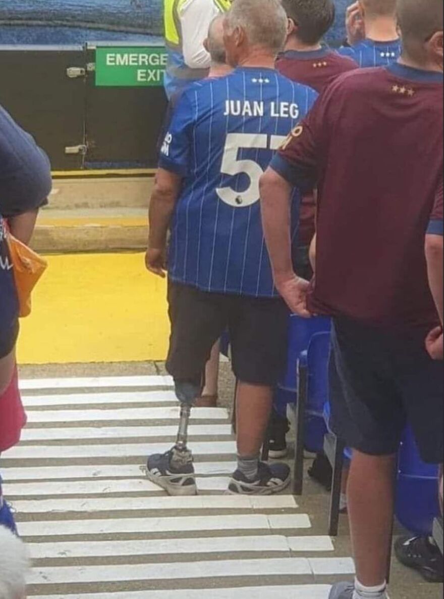 Man with prosthetic leg wearing a football jersey stands among fans; a humorous scene from pics that go hard.