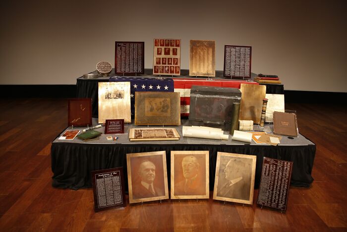 Historical time capsules display with photographs, documents, and artifacts on wooden floor.