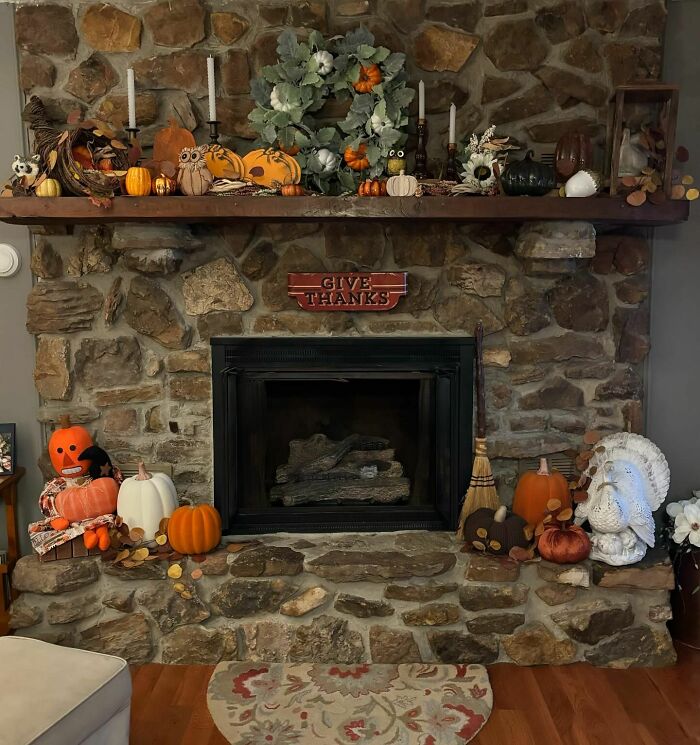 Thanksgiving home decoration with pumpkins and a "Give Thanks" sign on a stone fireplace mantel.