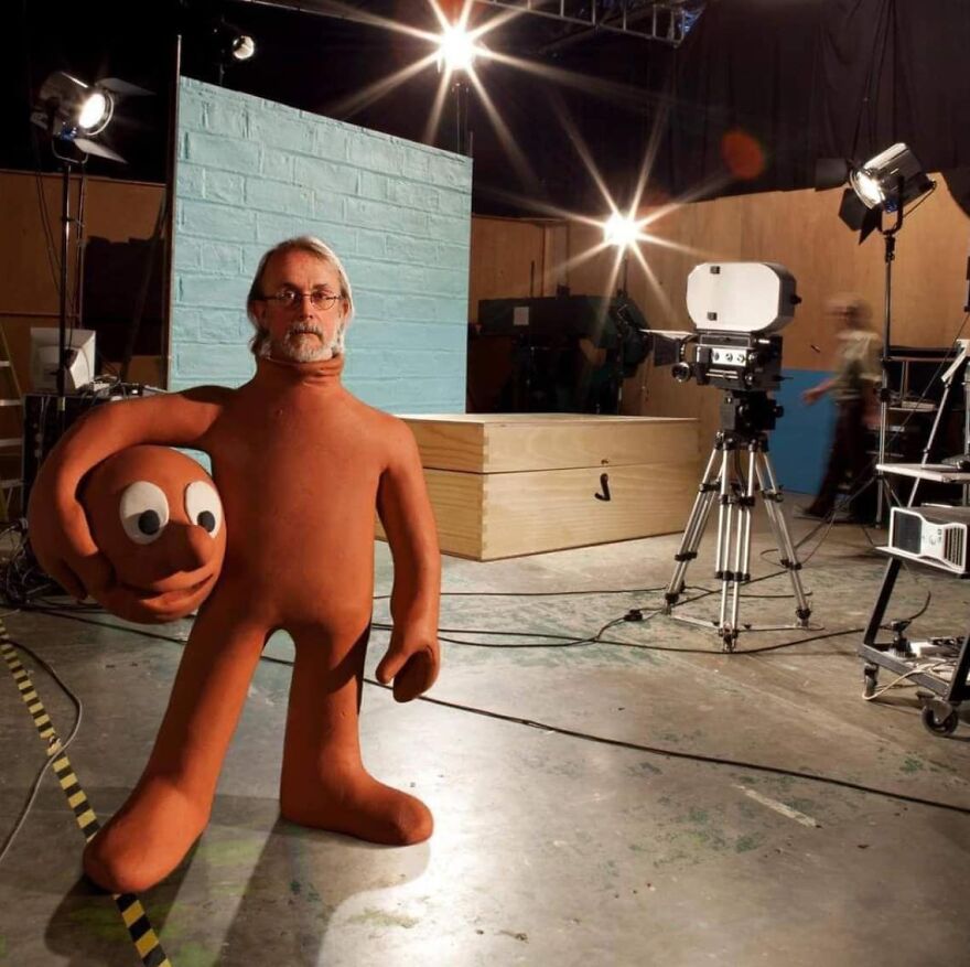 Man in a clay suit holding a large clay head, on a movie set with professional lighting and camera equipment; pics that go hard.