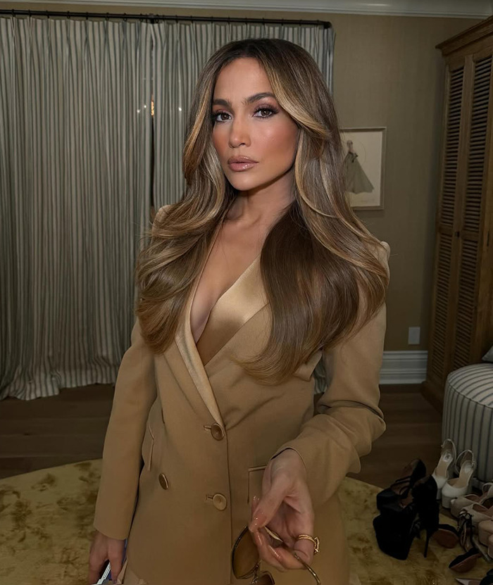 Jennifer Lopez in a beige suit, indoors, showcasing long hair and polished makeup.