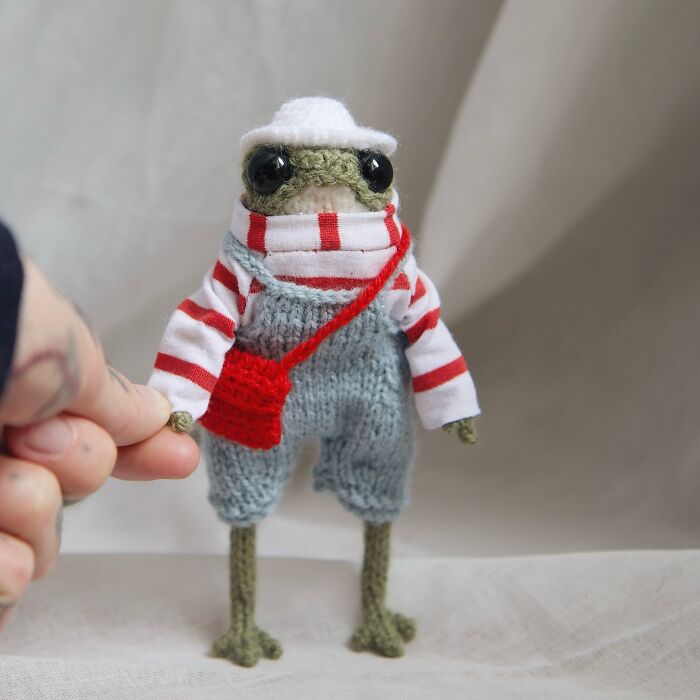 Miniature knitted frog in a striped shirt and overalls, showcasing cute artistry.