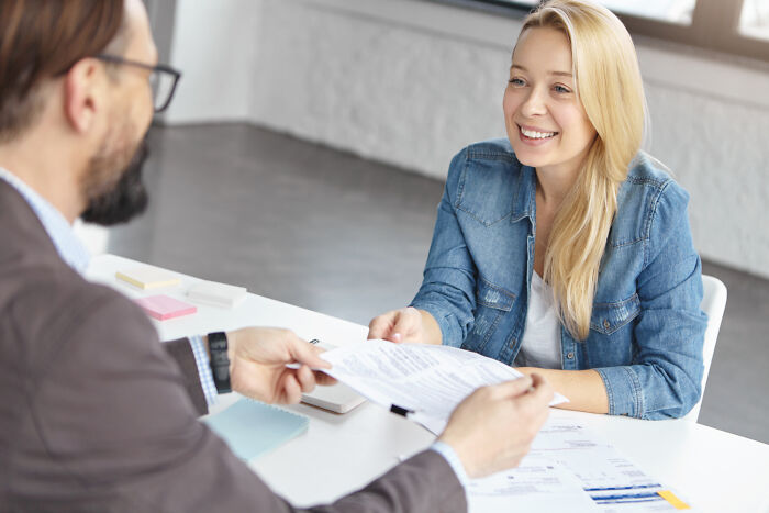 A woman in a denim jacket smiling while discussing a document with a man, illustrating risky decision outcomes.