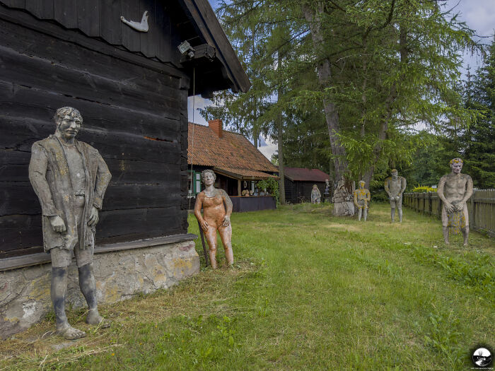 Sculptures by Adam Szubski in a rustic outdoor setting surrounded by trees and wooden buildings.