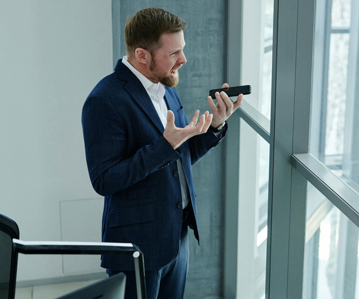 Man in blue suit on a call, gesturing with frustration, illustrating malicious compliance. Man in blue suit on a call, gesturing with frustration, illustrating malicious compliance.