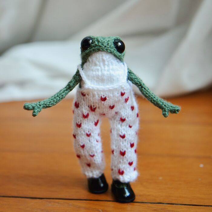 Knitted miniature frog wearing white pants with red hearts, created by a French artist