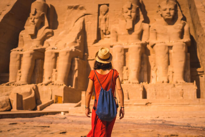 Woman in red dress and hat exploring ancient statues, symbolizing Americans experiencing reverse culture shock abroad.