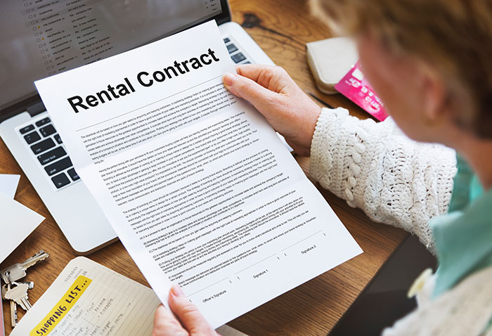 Person reviewing a rental contract over a laptop, emphasizing the importance of reading the fine print before signing.